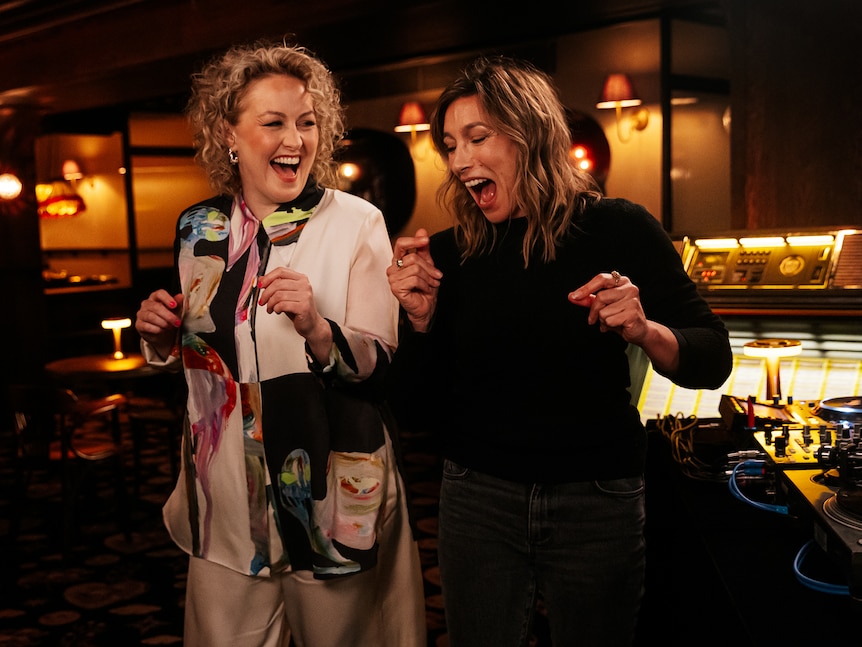 Zan Rowe and Claudia Karvan dancing and laughing in a dimly lit nightclub