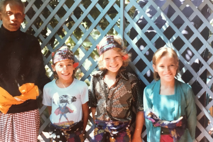 Three children pose in Bali, wearing traditional Indonesian clothing.